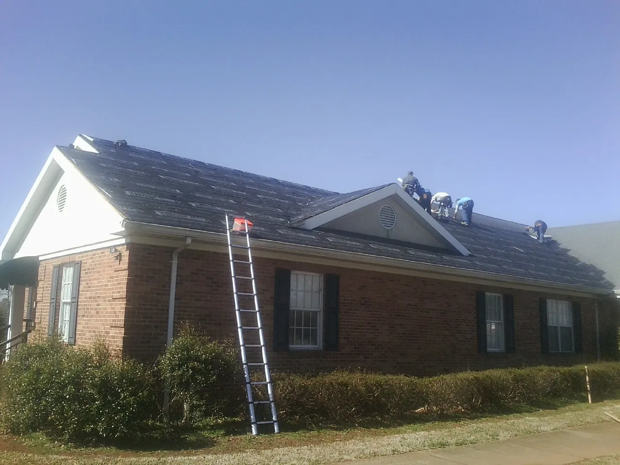 Crew tearing shingles off a brick ranch roof with a ladder set — Emergency Roof Repair work by our crew in Vickery
