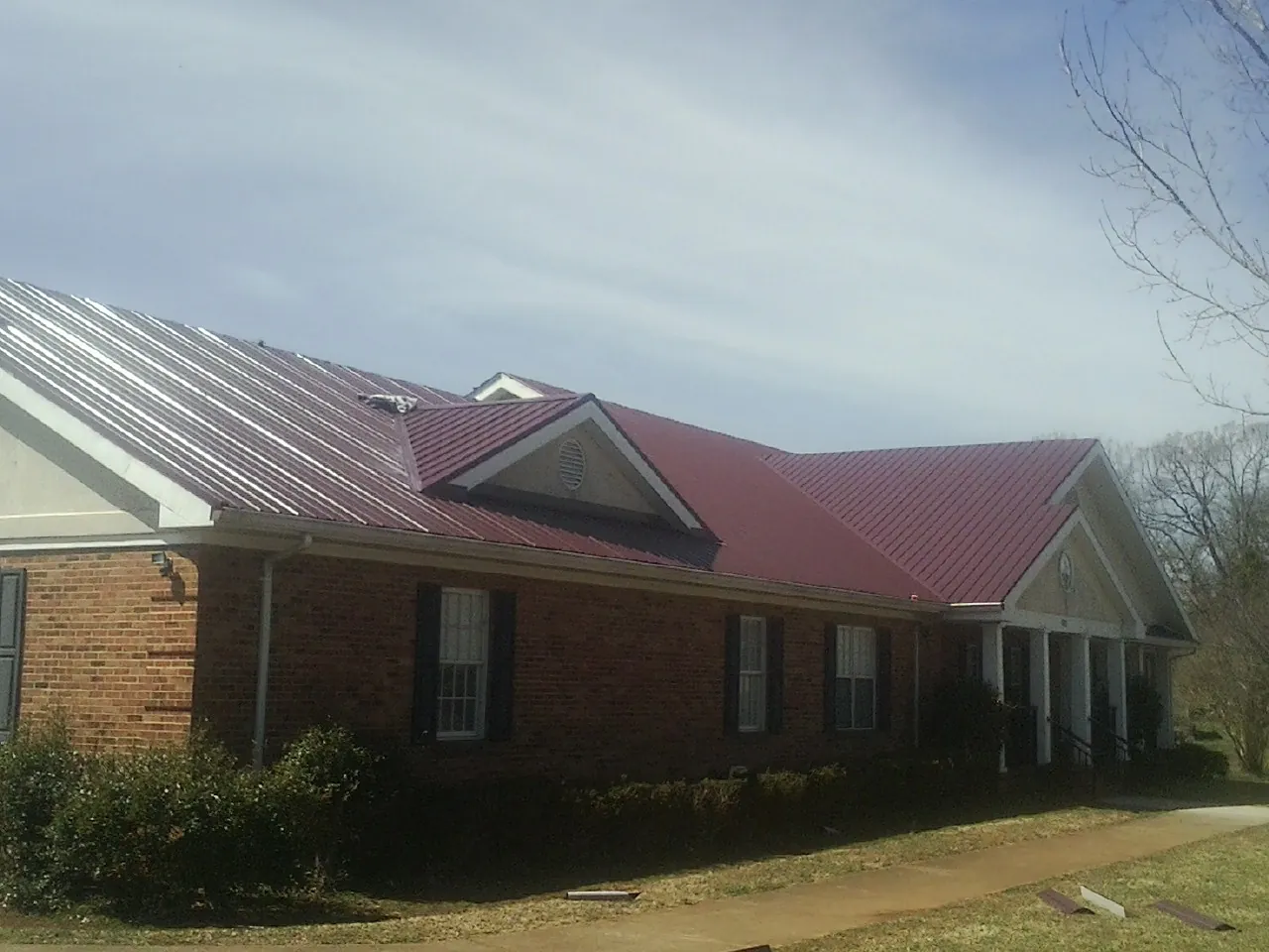 Red metal roof with gabled entries on a long brick building, from a Hail Damage Roof Repair job in Vickery