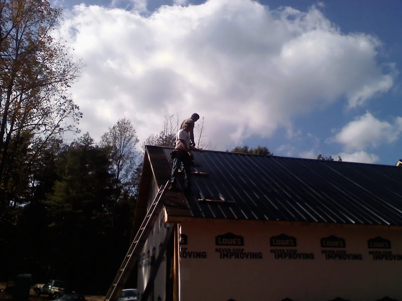 Roofer fastening dark metal panels high against a cloudy sky, from a Roof Inspection job in Vickery