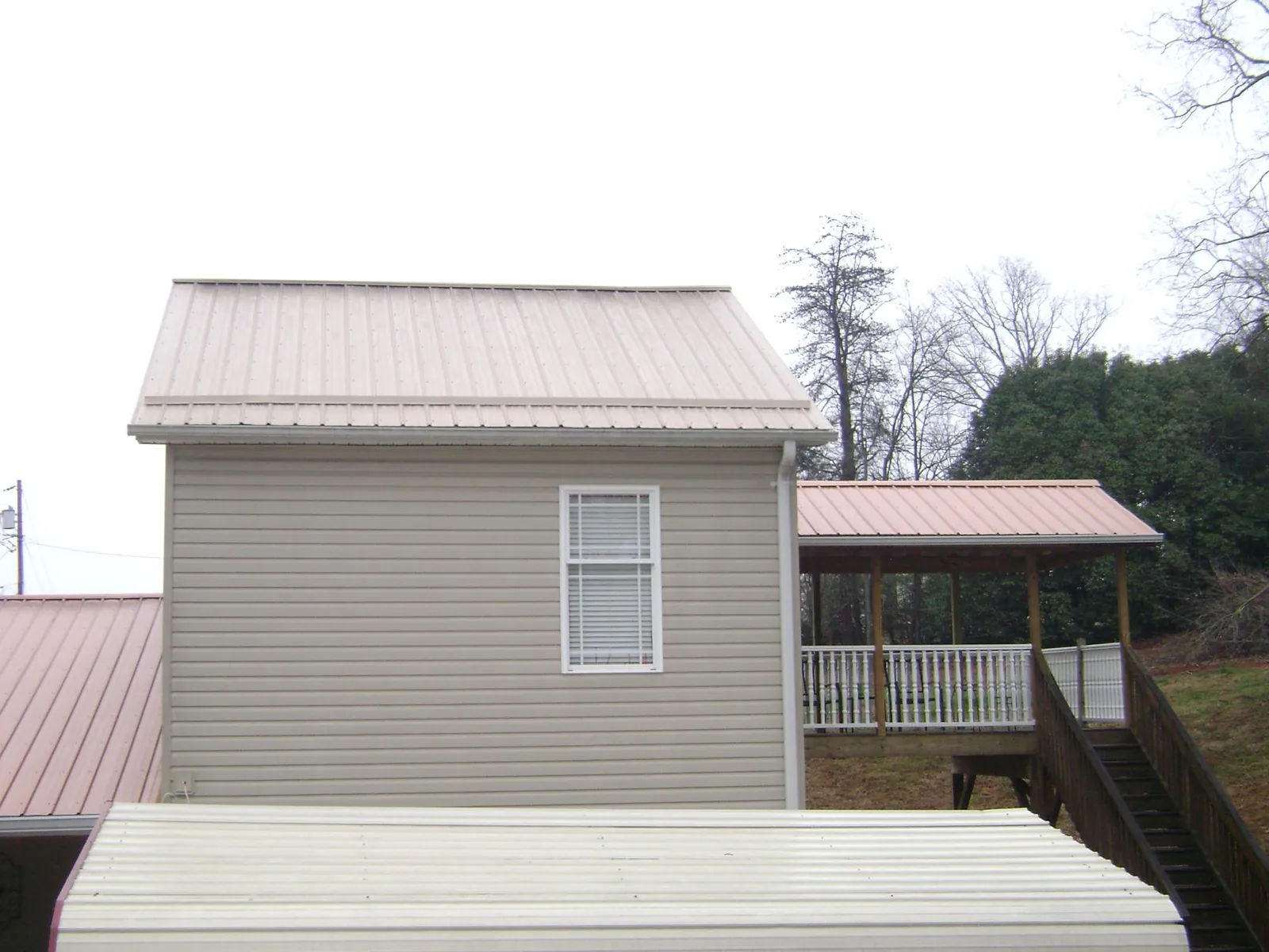 Tan metal roofs on a two story addition and attached porch, from a Roof Replacement job in Vickery